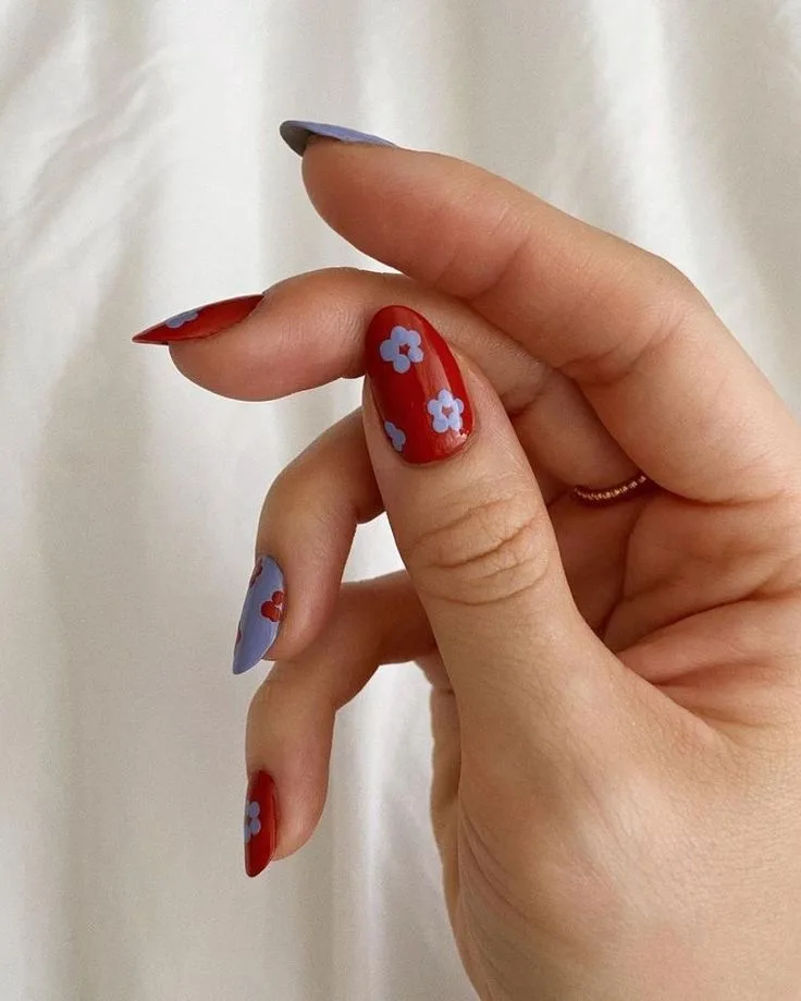 Red and lilac floral August nails featuring vibrant flowers in rich red and soft purple hues.
