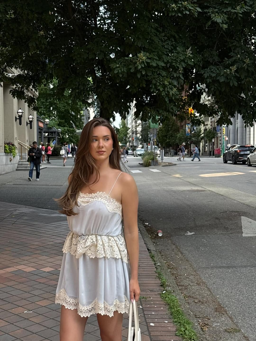 Woman in silver-blue satin lace-trim cami and matching micro shorts with white tote bag on a city street.