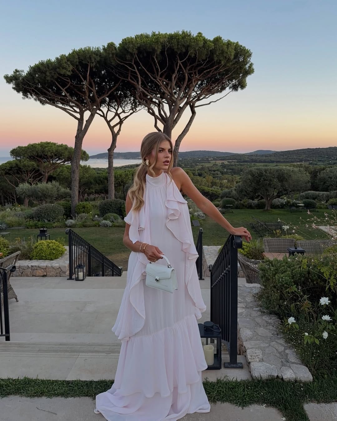 Woman in blush pink halterneck cascading ruffle maxi gown with mint mini bag at a South of France wedding.