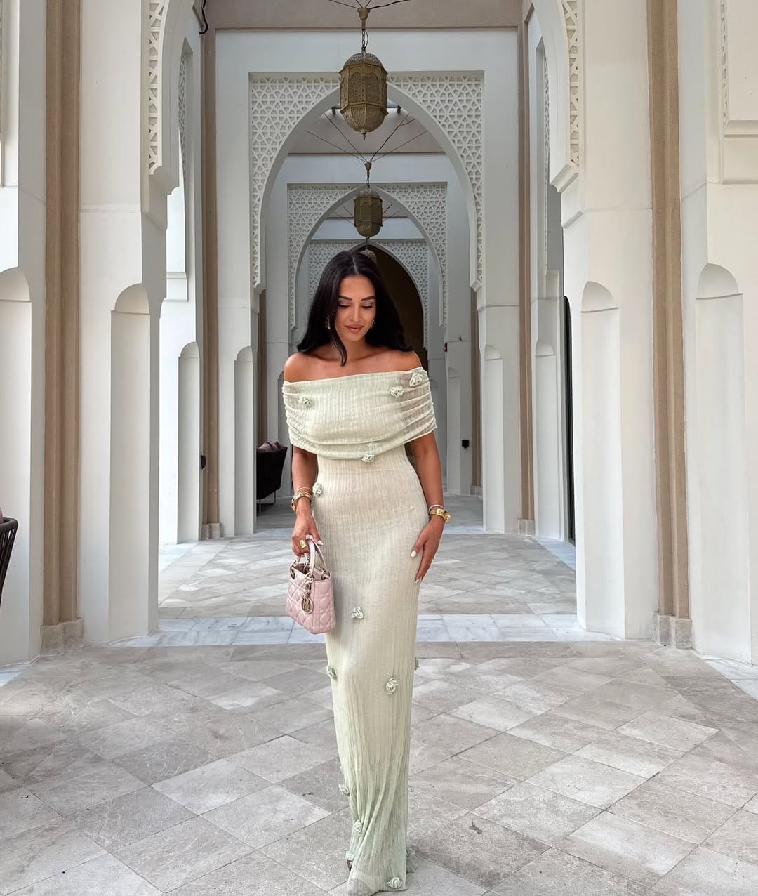 Woman in ivory off-shoulder ribbed column maxi with 3D floral appliqué and pink Lady Dior bag in a Moorish corridor.
