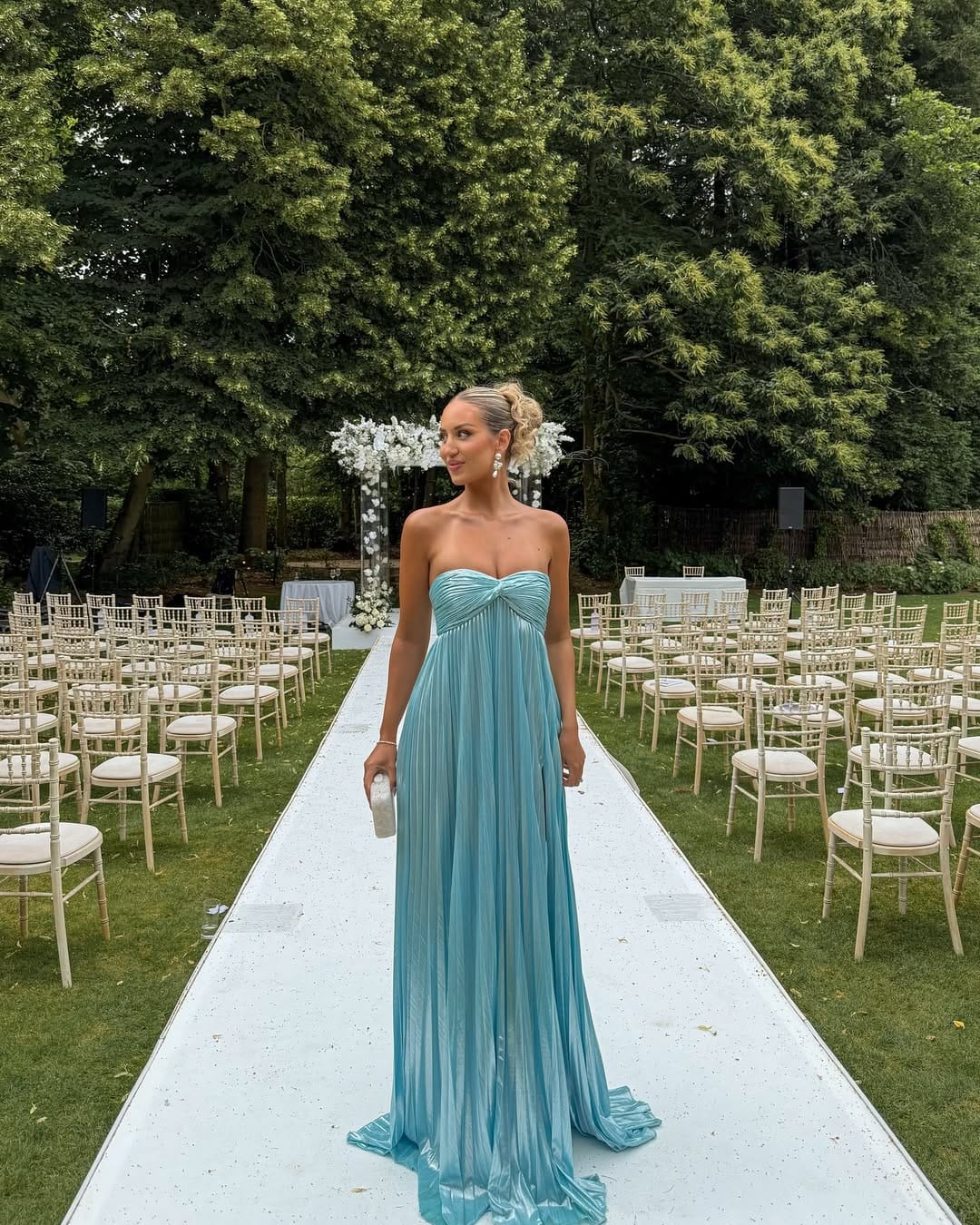 Woman in aqua blue metallic pleated strapless empire-line maxi gown on a white aisle at an outdoor garden wedding.