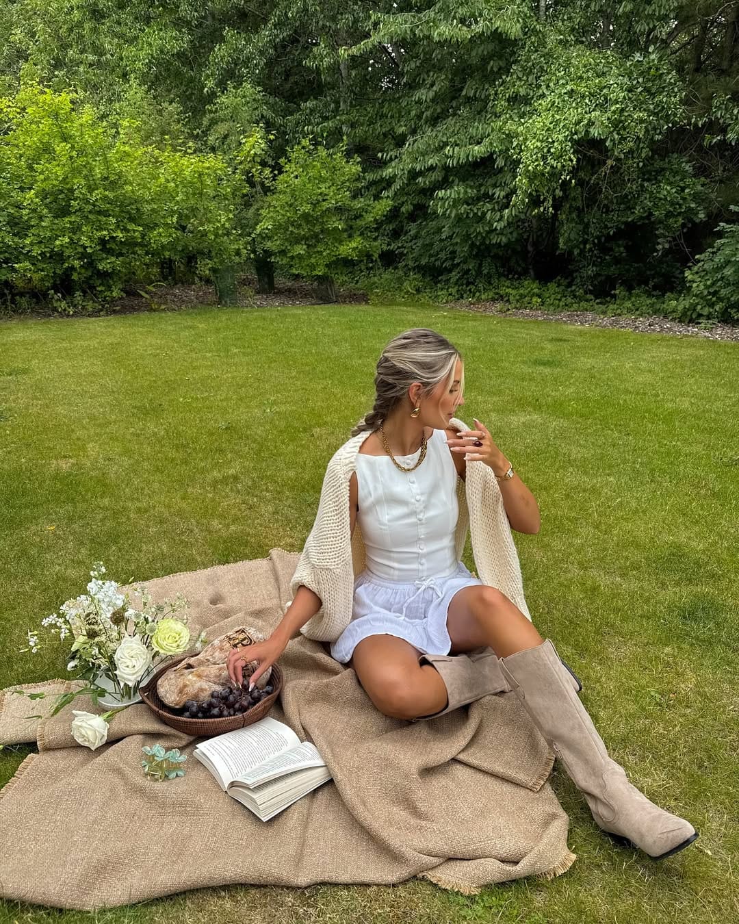 White linen mini dress layered with a cream knit cardigan and suede knee boots