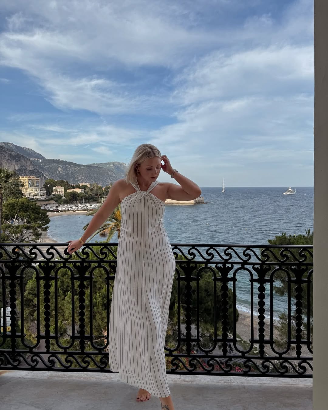 White pinstripe halter twist-front maxi dress on hotel balcony overlooking sea beach outfit idea