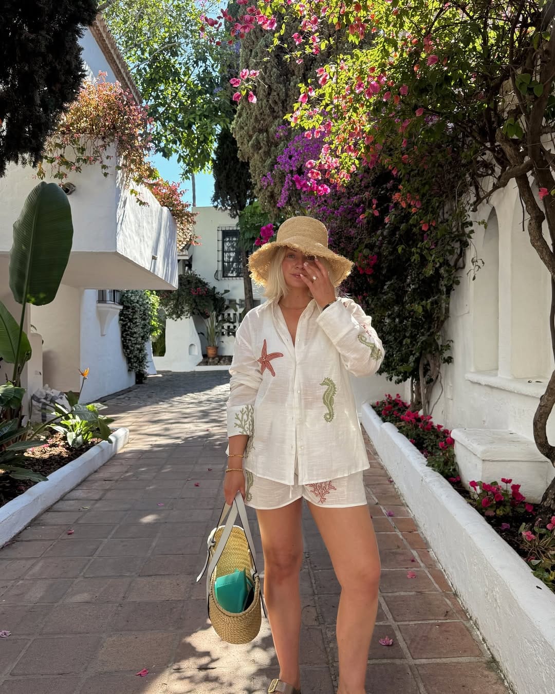 White marine-embroidered linen shirt and shorts co-ord with straw bucket hat beach outfit idea