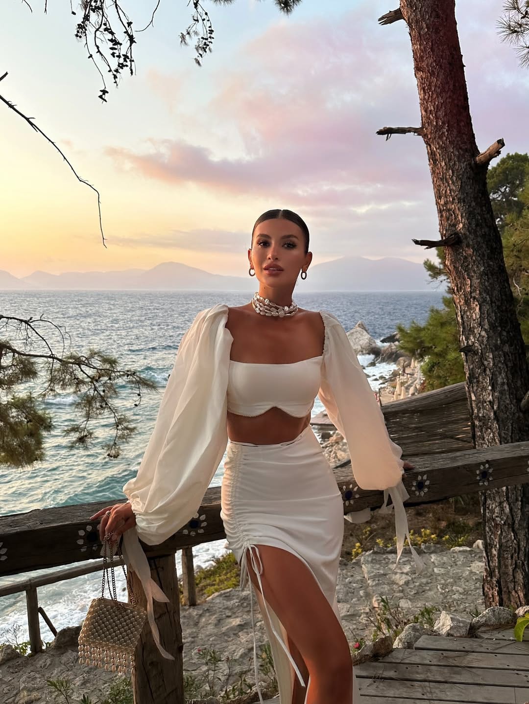White balloon-sleeve crop top and ruched mini skirt with pearl choker beach outfit idea at sunset