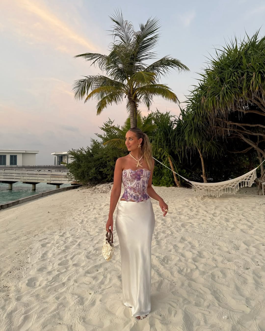 Purple printed corset top with white satin maxi skirt and starfish necklace on beach at sunset beach outfit idea