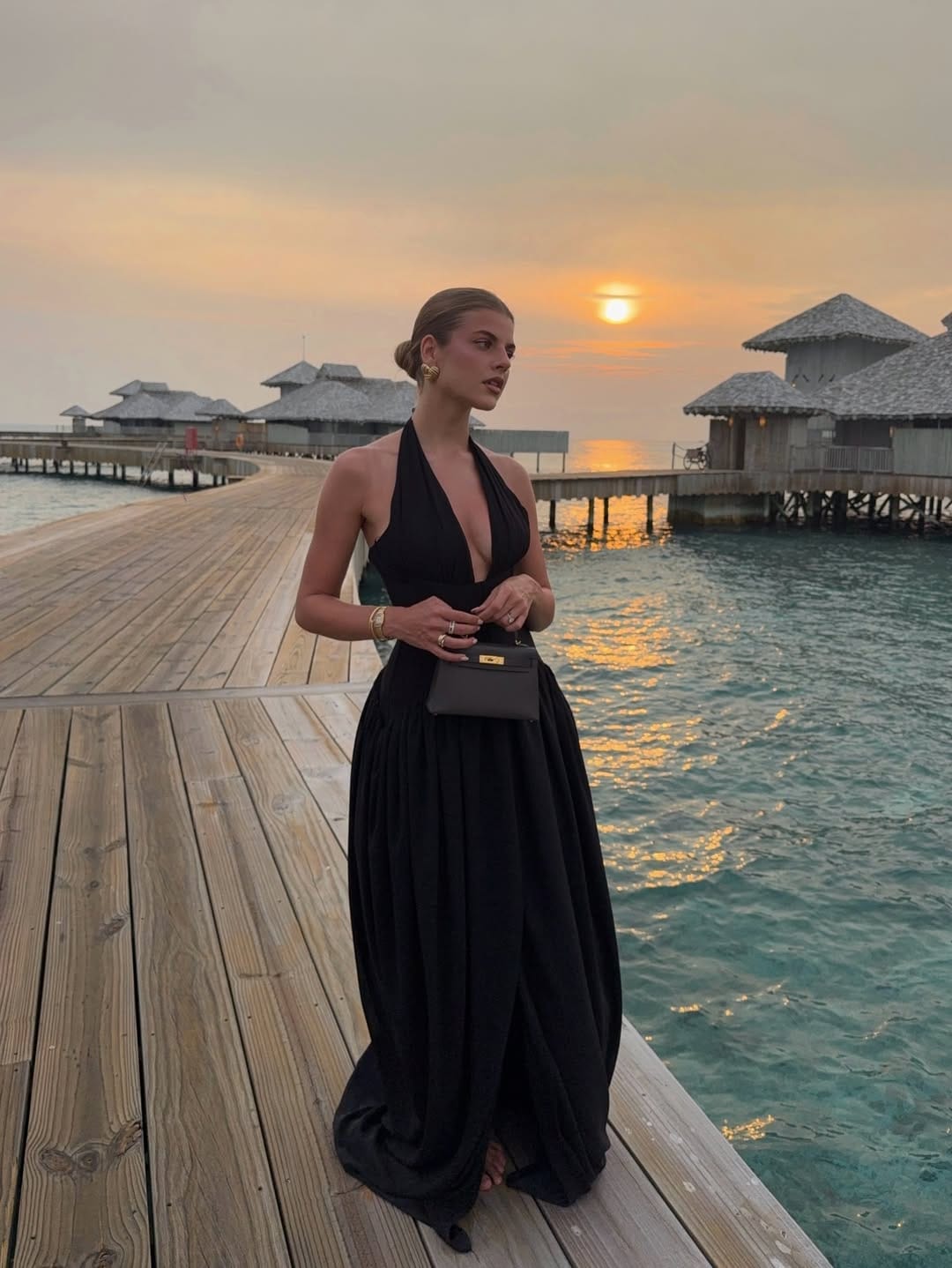 Black deep-V halter full-skirt maxi dress with HermĆØs Kelly bag on Maldives overwater jetty beach outfit idea