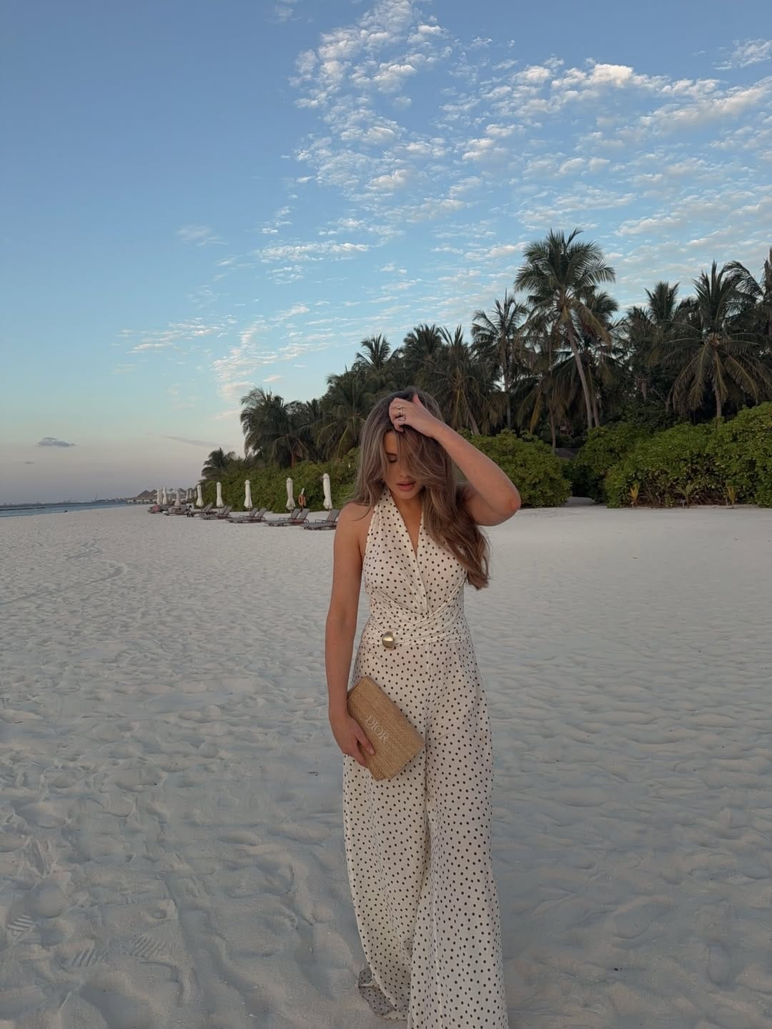 Cream polka dot halter wrap jumpsuit with Dior straw clutch on white sand beach outfit idea