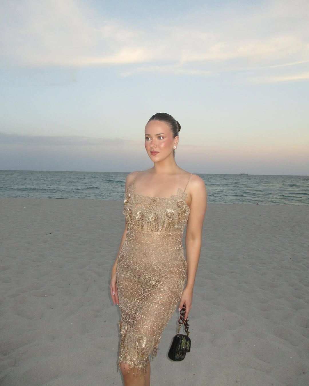 Gold lace embellished spaghetti-strap midi dress with dark bag on beach at sunset beach outfit idea