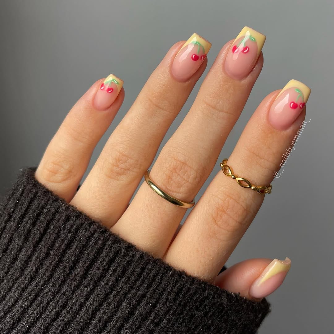 Butter yellow French tip nails with cute cherry accents for a playful summer look