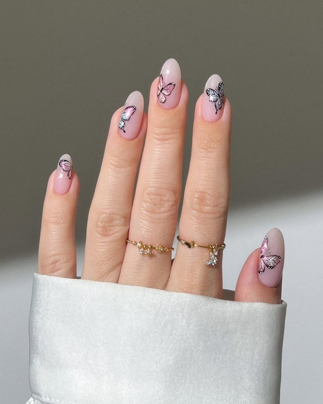Sheer blush almond nails with scattered iridescent butterfly accents