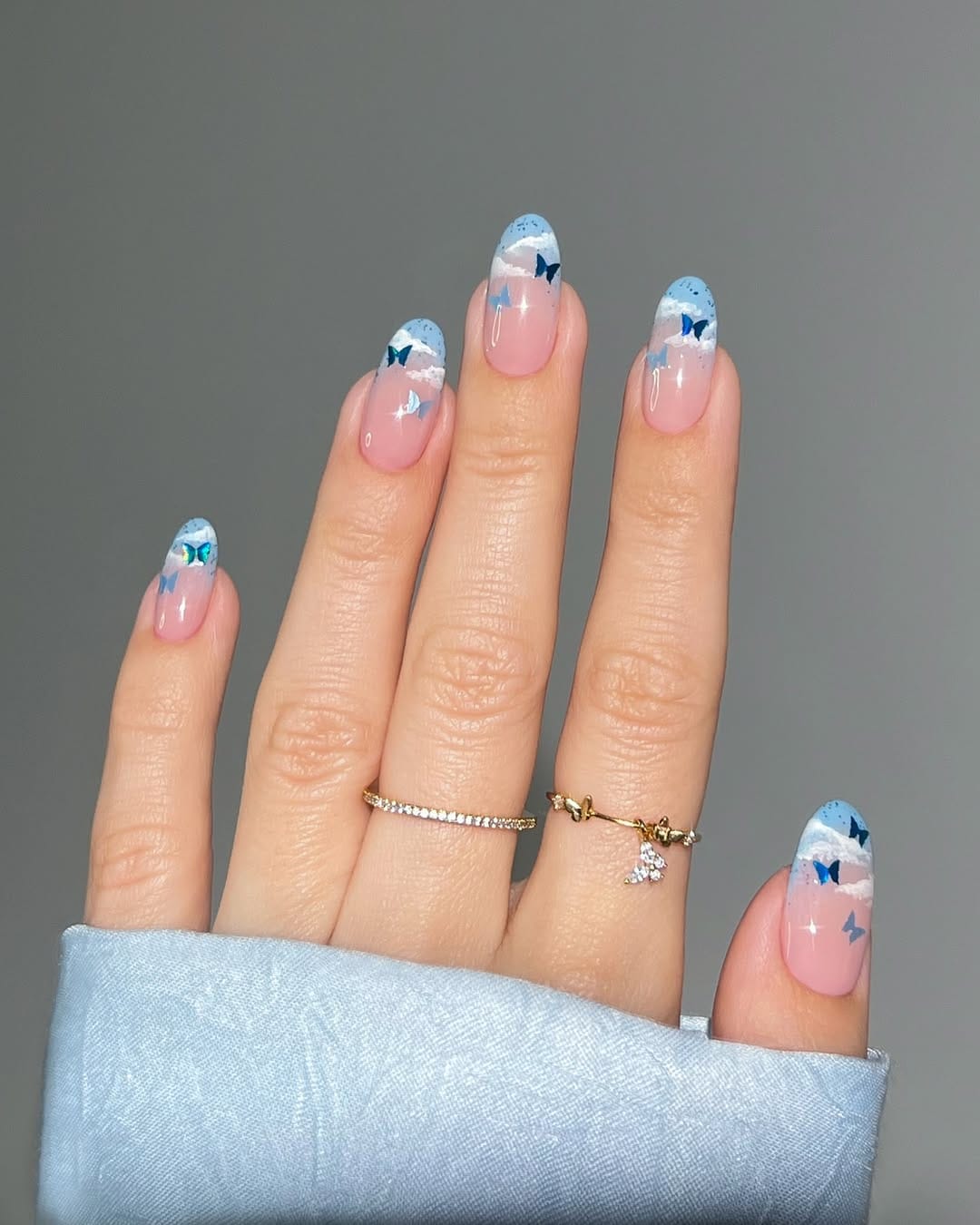 Sheer blush almond nails with sky and cloud French tips and butterfly details