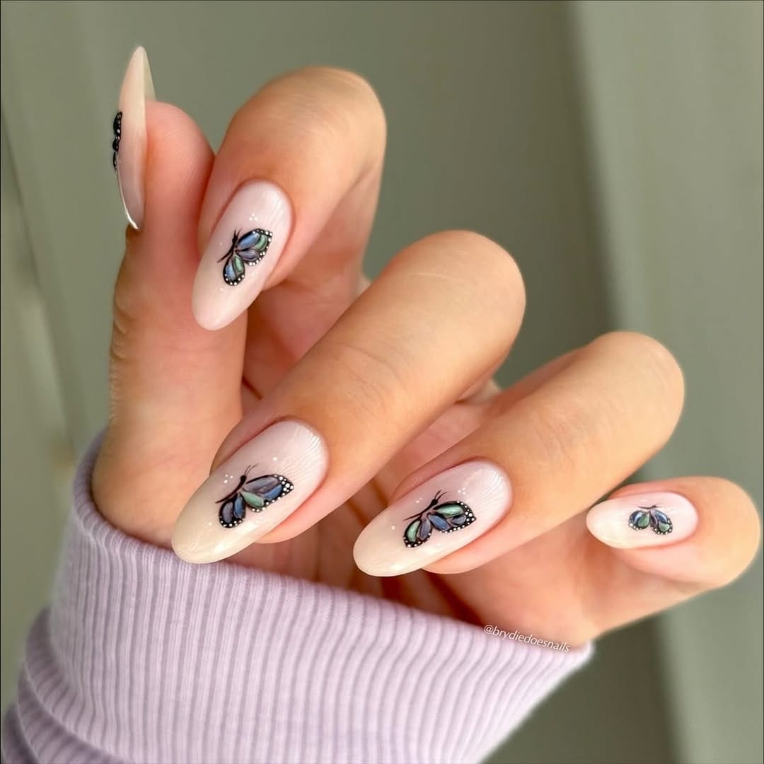 Sheer nude almond nails with duochrome blue-green butterfly design