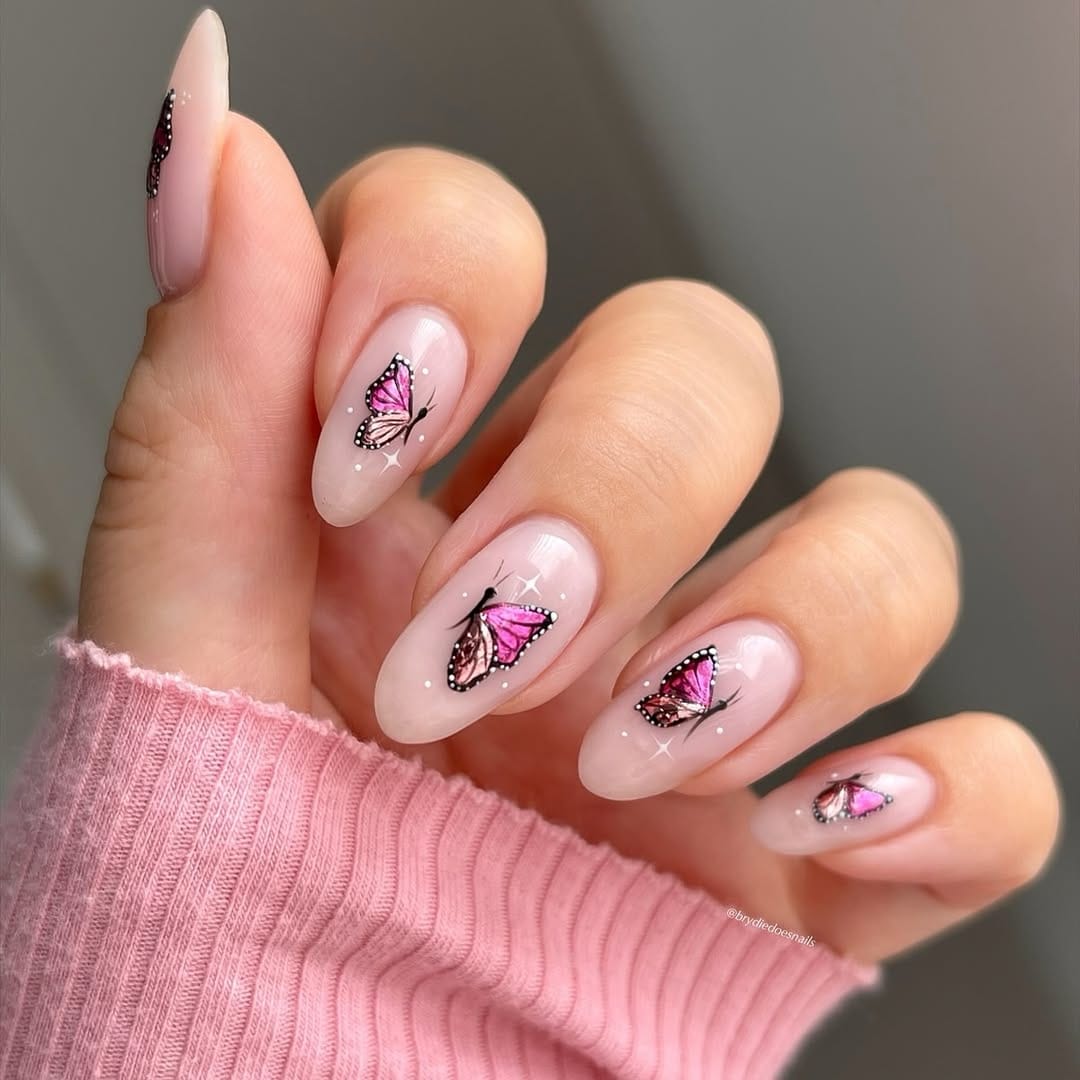 Sheer nude almond nails with pink monarch butterflies and sparkle detail