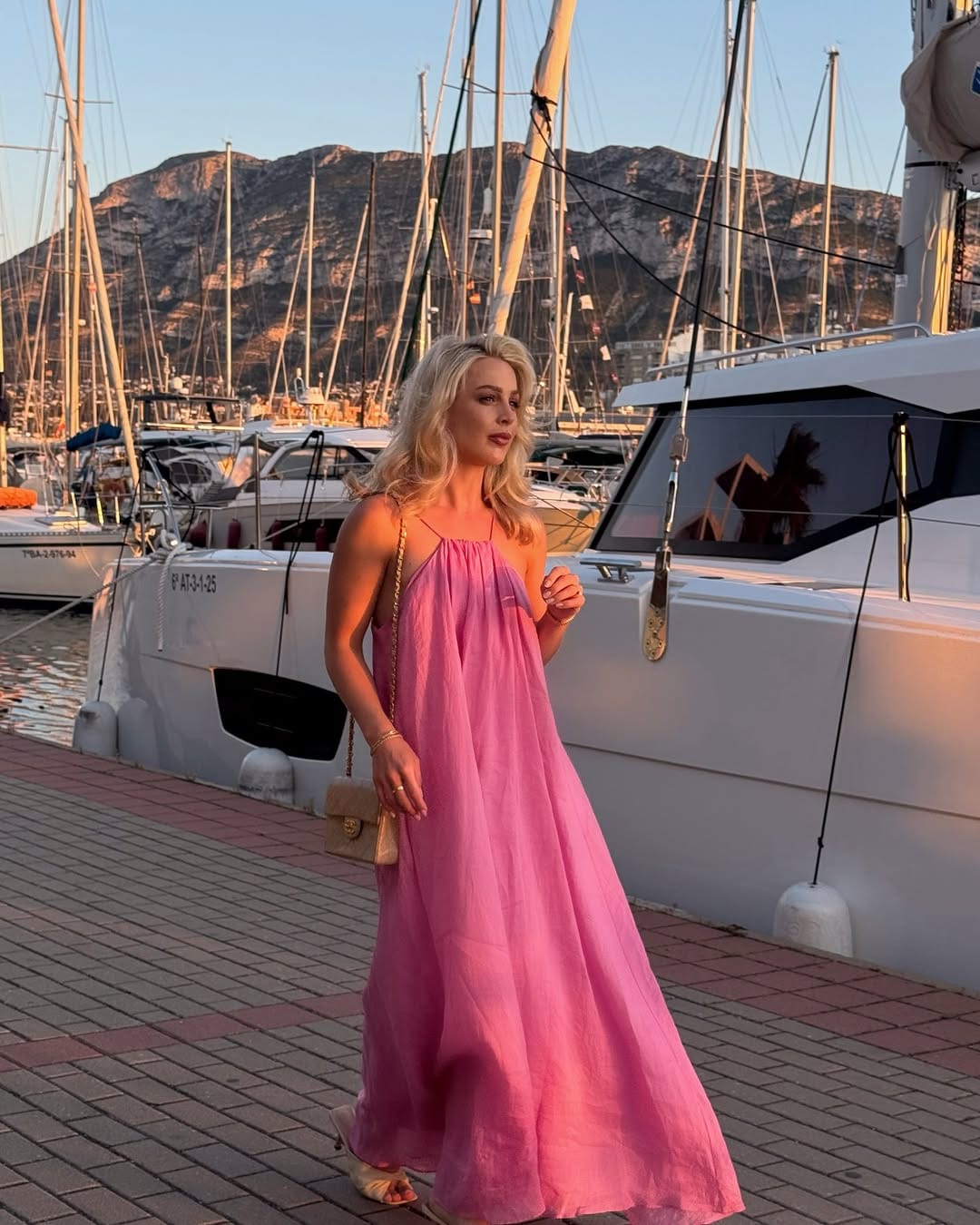 Pink chiffon maxi dress with spaghetti straps and gold Chanel bag at a marina at sunset