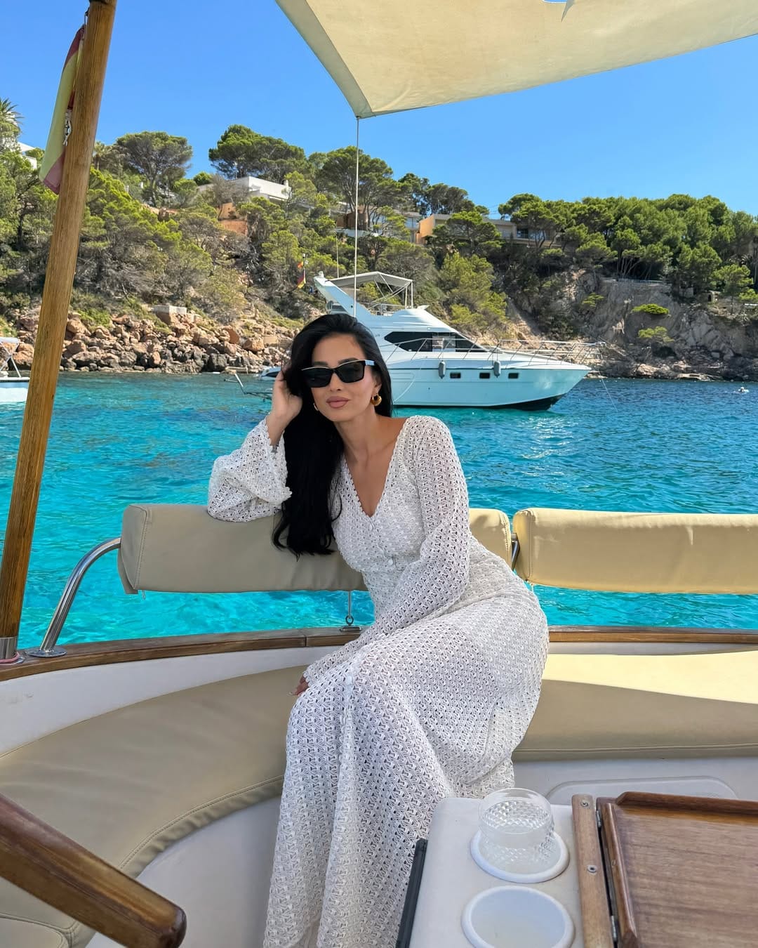 White long-sleeve crochet wrap maxi dress with gold hoop earrings on a wooden boat in Mallorca