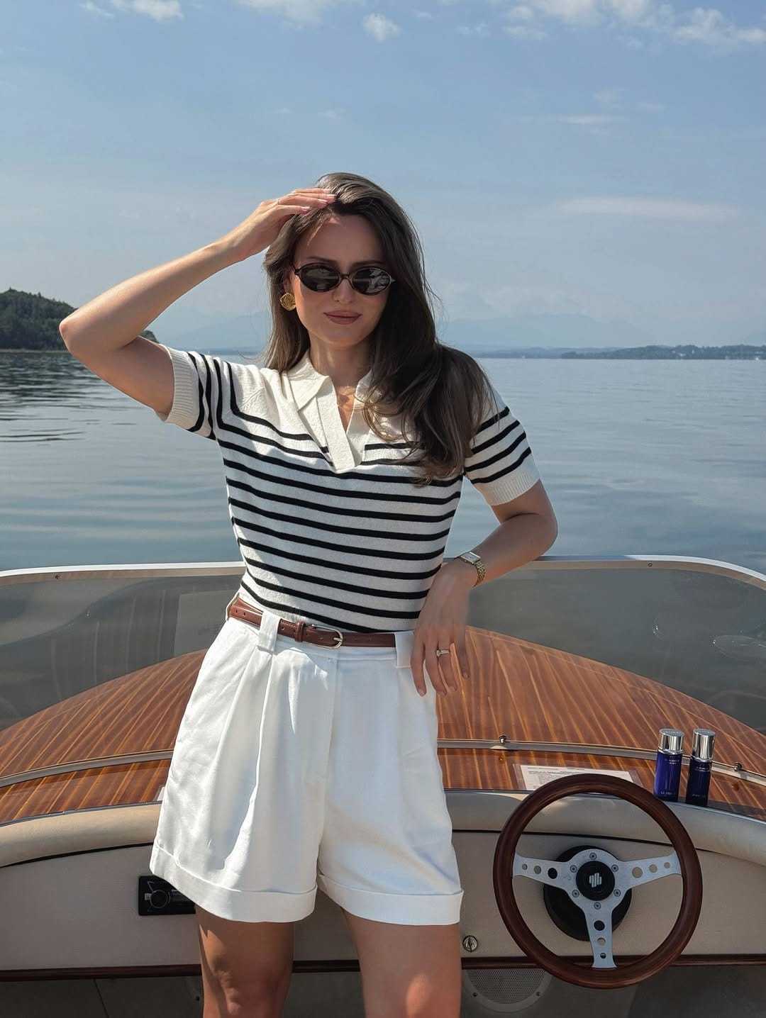 Cream and black Breton stripe knit polo with white tailored cuffed shorts and tan belt on a wooden speedboat