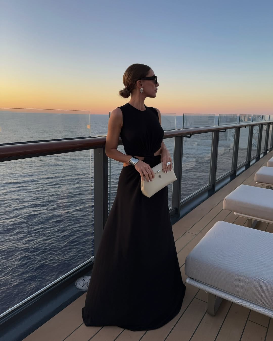 Black sleeveless crop top and full A-line maxi skirt co-ord with cream clutch on a cruise ship at sunset