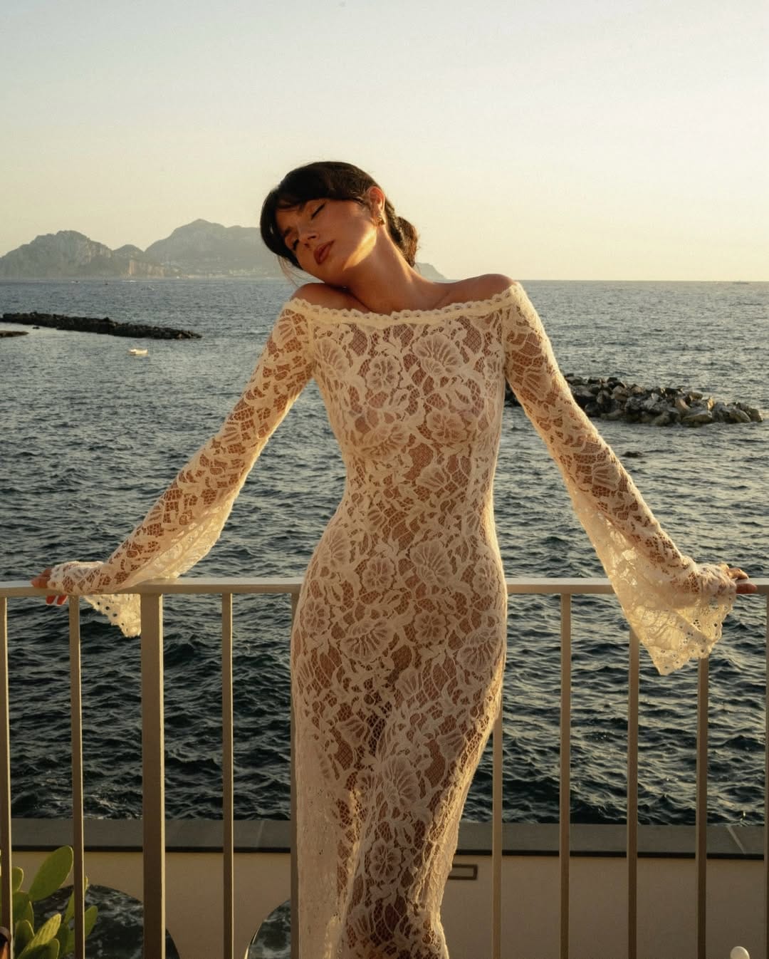 Cream off-shoulder floral lace maxi dress with flared sleeves on a Mediterranean balcony at golden hour