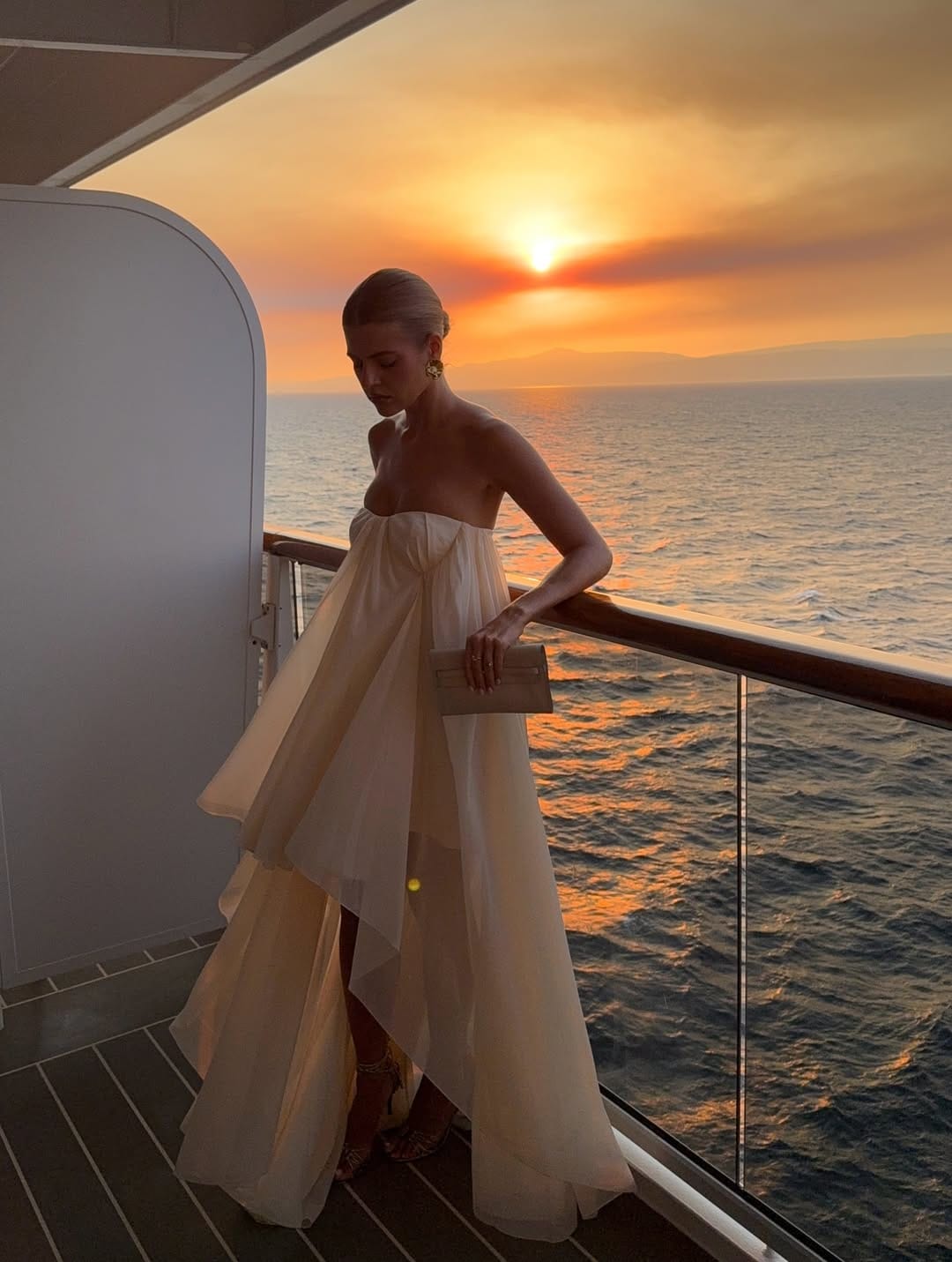 Champagne strapless tiered organza gown with asymmetric hem and strappy heels on a cruise ship deck at sunset