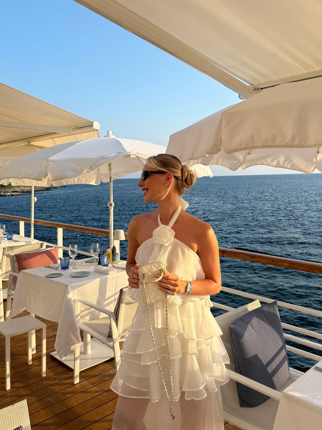 White halter ruffle mini dress with three-dimensional rose neckline and white Chanel bag at a waterfront restaurant