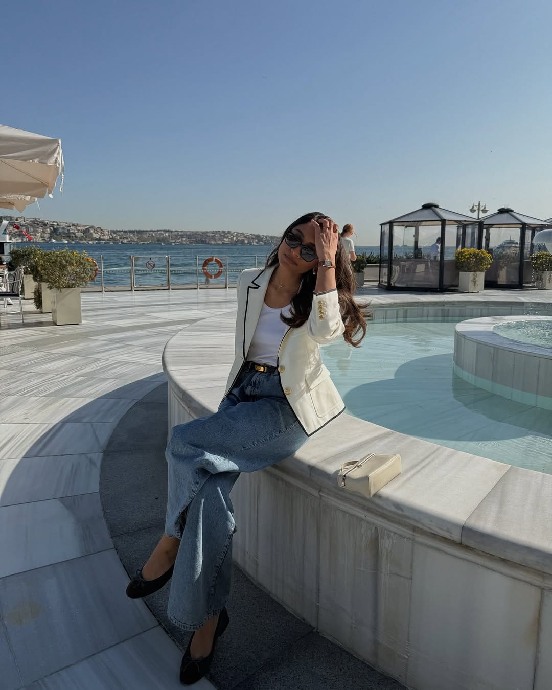 White blazer with black piping trim and gold buttons over white tank and wide-leg jeans by the Bosphorus