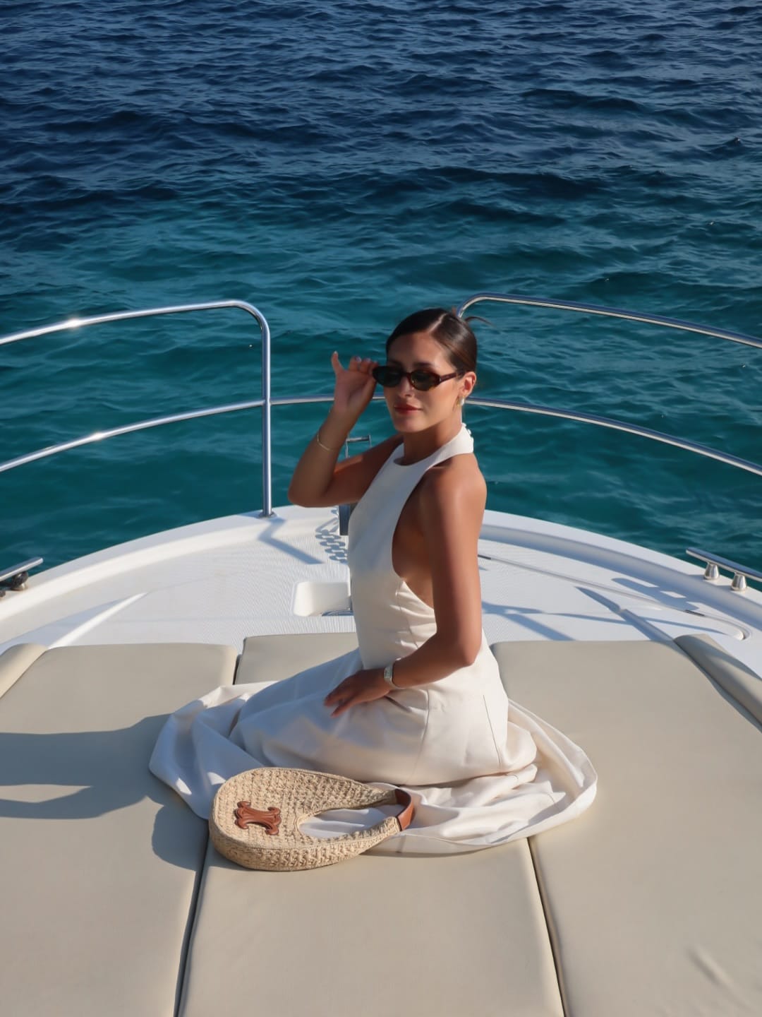 Cream halterneck midi dress with open back and raffia tote bag on a yacht deck