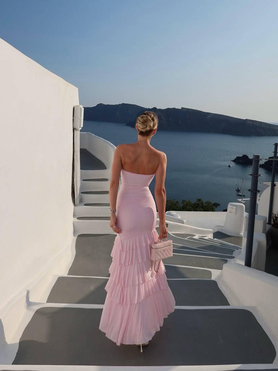 Pink strapless tiered ruffle maxi dress with quilted bag on Santorini Greece caldera steps