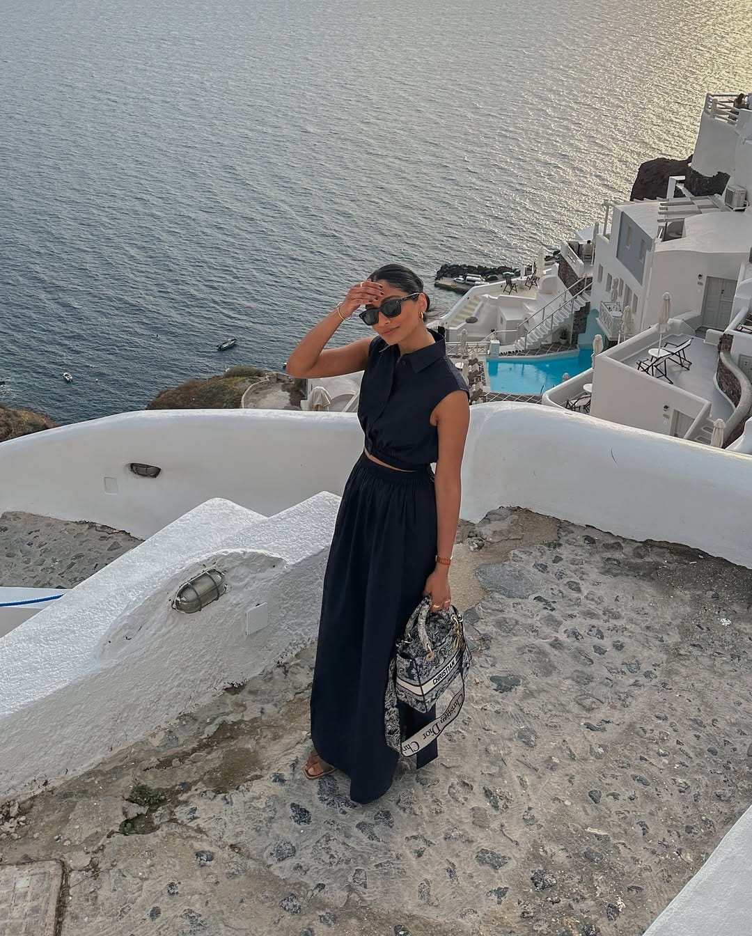  Black cropped shirt and black wide-leg maxi skirt with Dior saddle bag overlooking Santorini Greece caldera