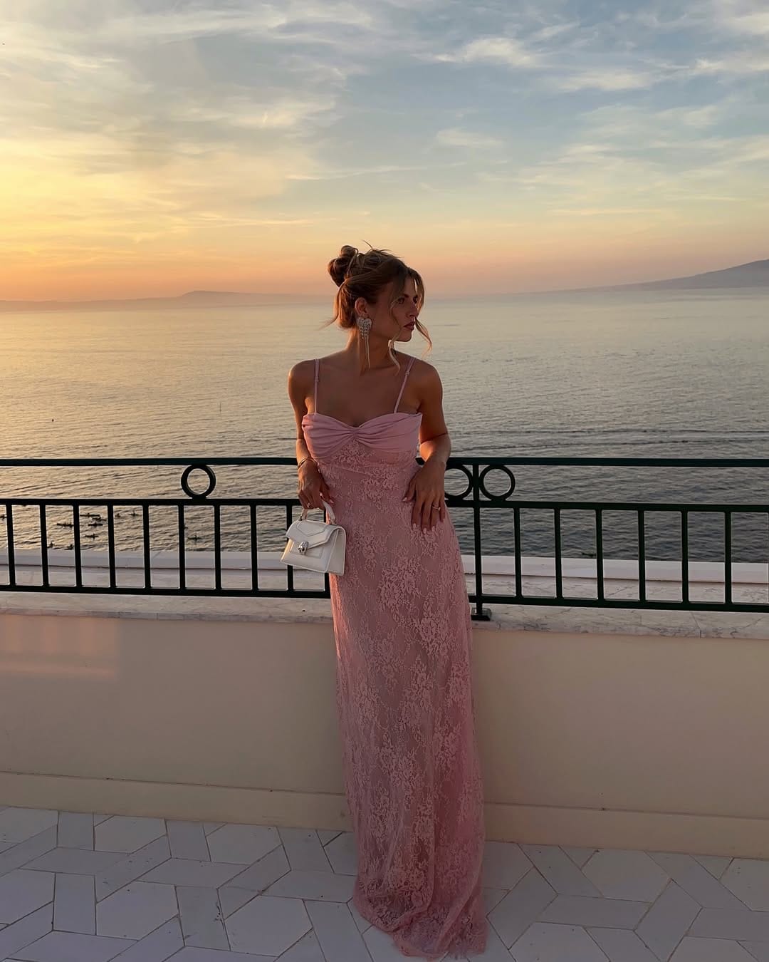 Pink lace column maxi dress with white Versace bag on Greece balcony at sunset