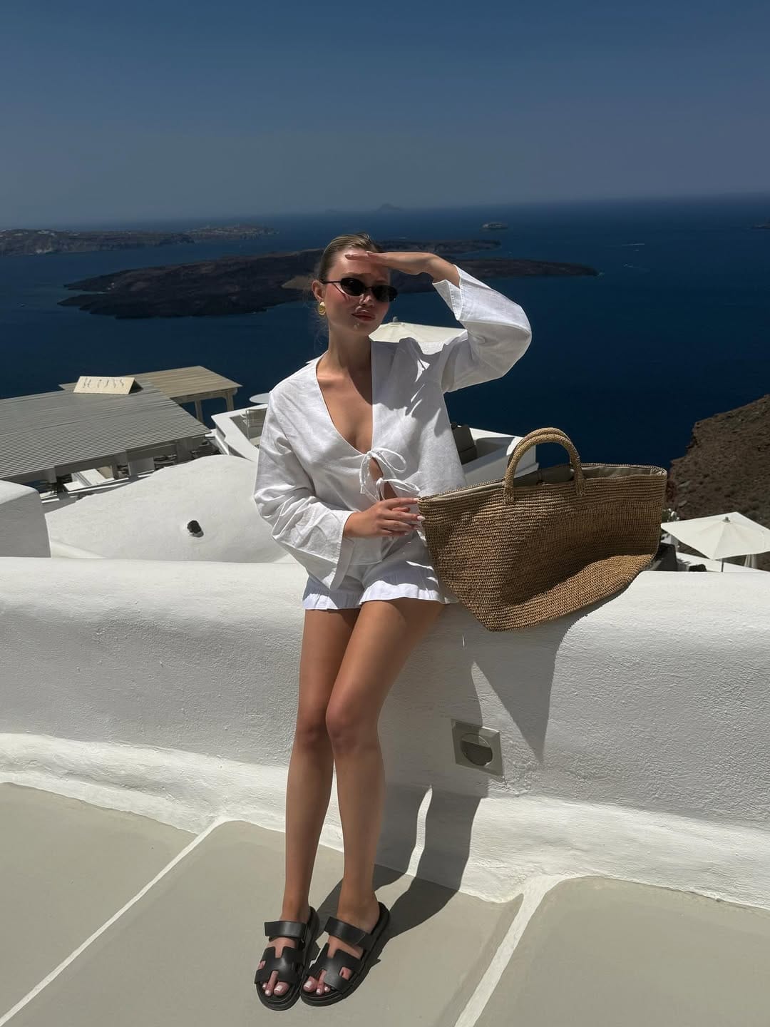 White linen tie-front top and shorts with straw tote on Santorini Greece whitewashed rooftop