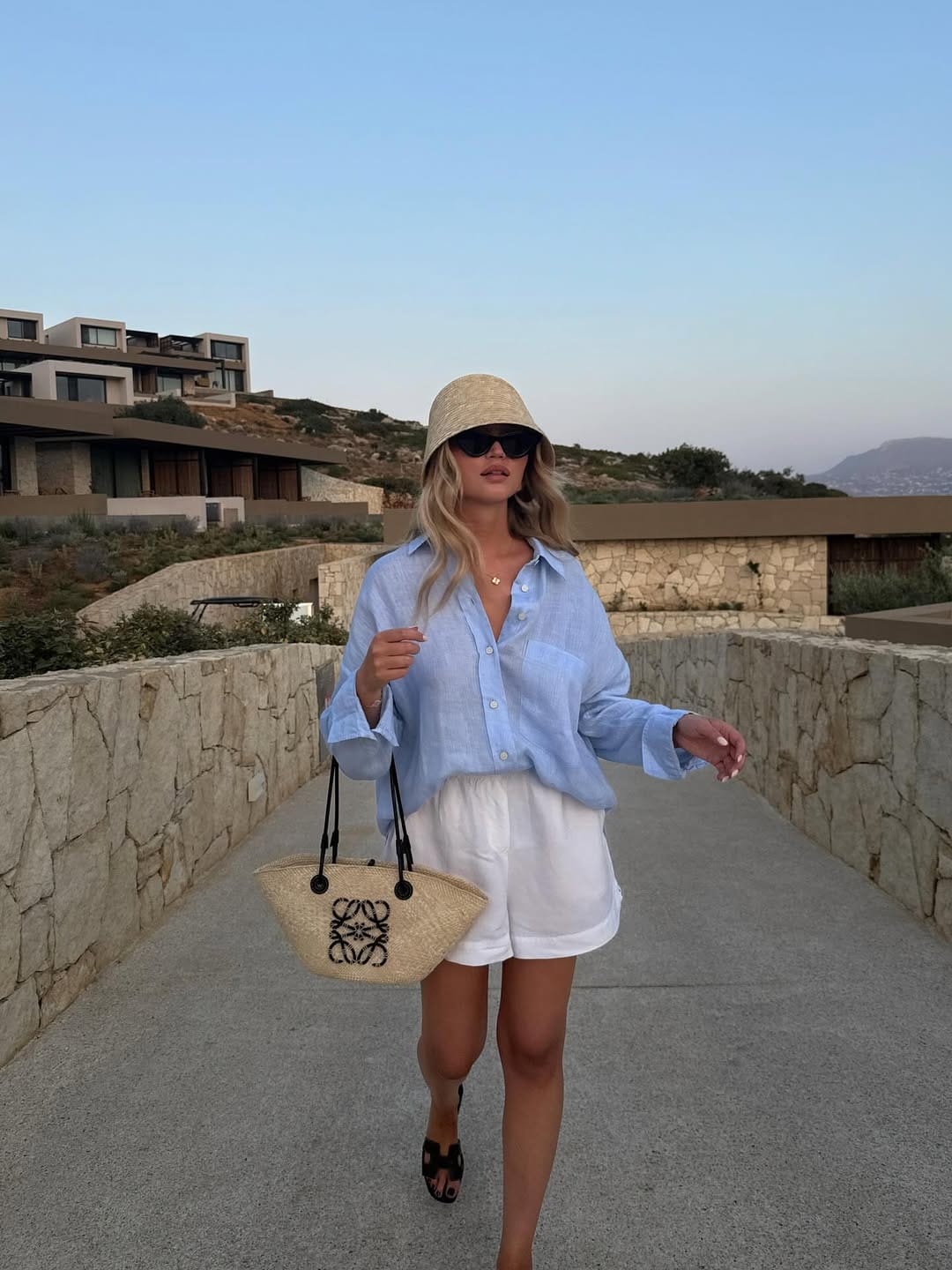  Blue linen oversized shirt and white shorts with Loewe straw bag and bucket hat in Greece
