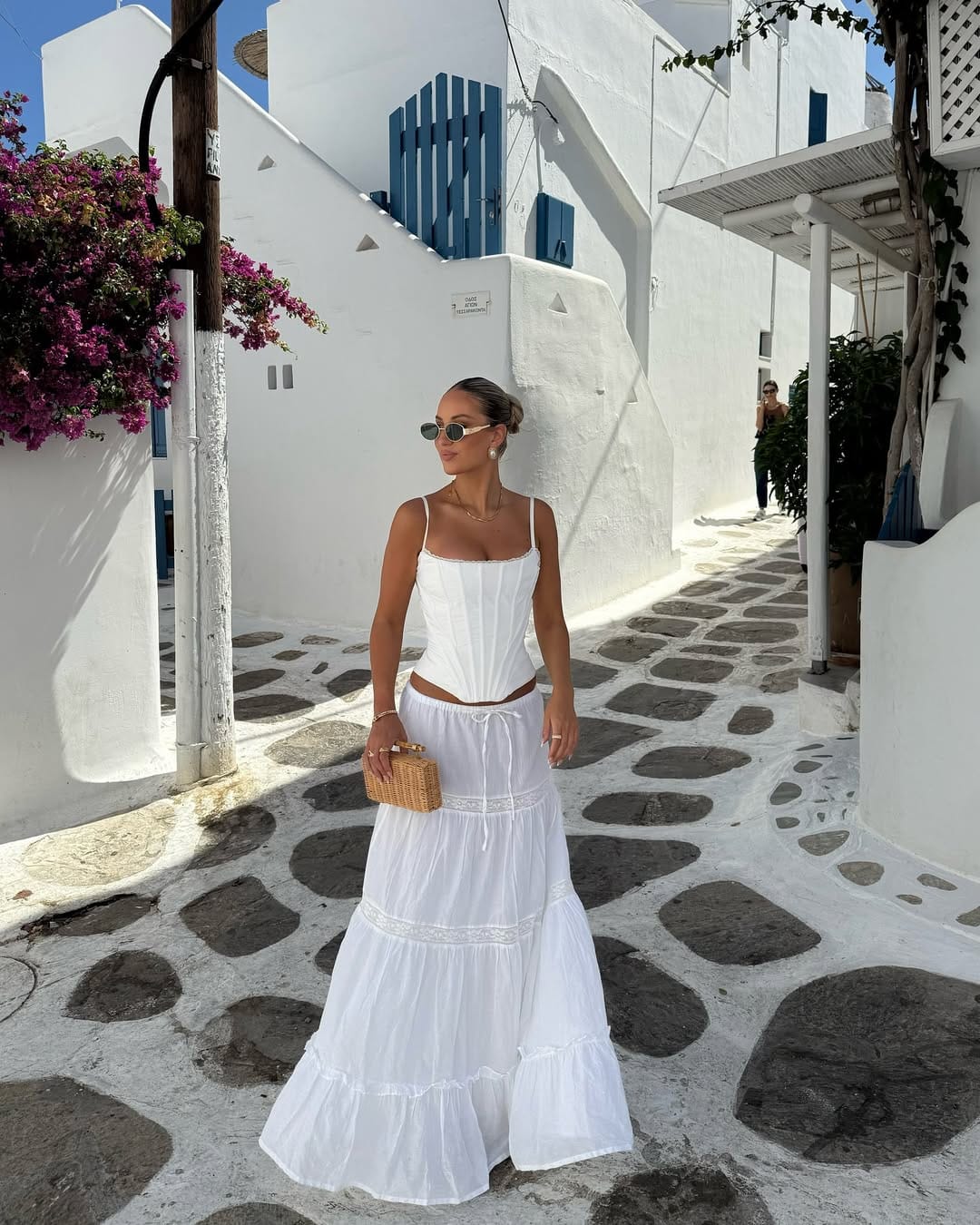 White corset top and tiered lace-trim maxi skirt with rattan clutch in Mykonos Greece Town