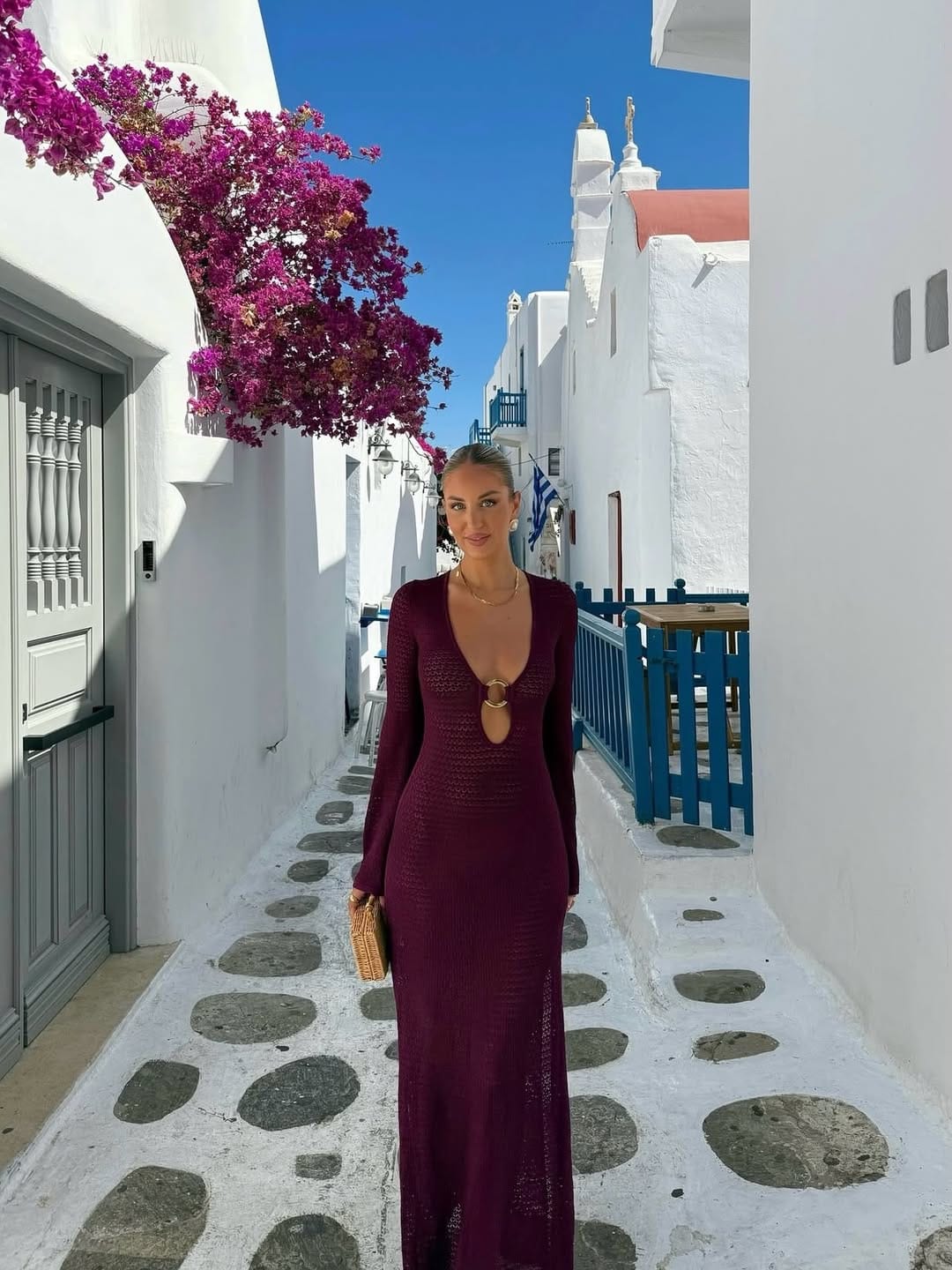 Burgundy crochet knit deep-V maxi dress with rattan clutch in Mykonos Greece bougainvillea alleyway