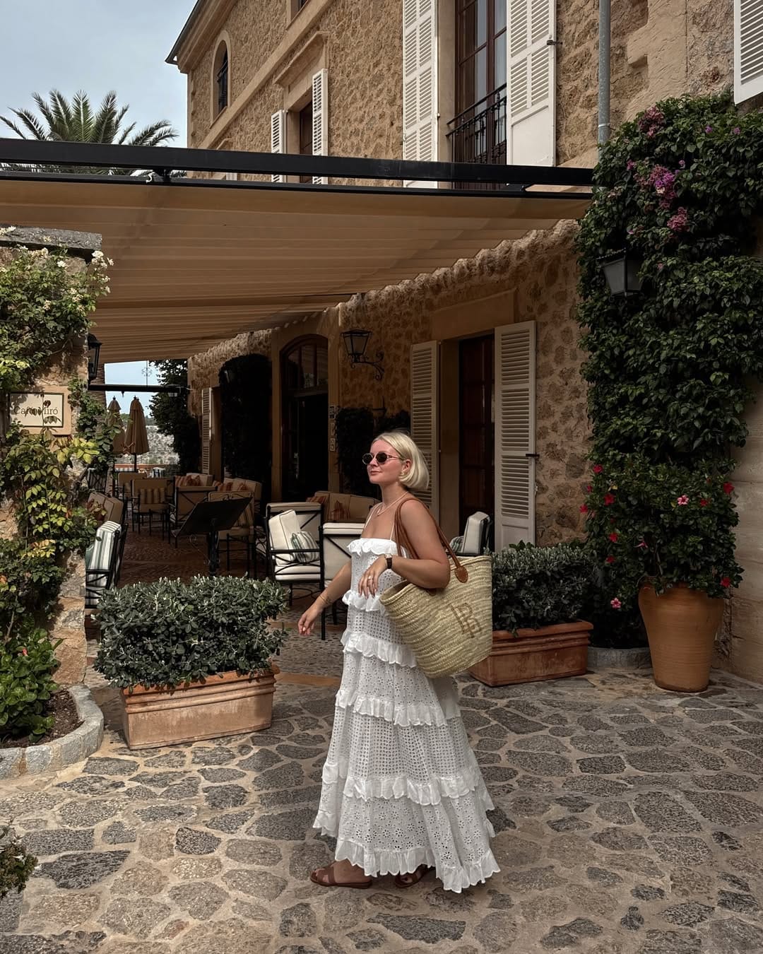 White broderie anglaise tiered maxi dress with straw tote and tan sandals outside a stone villa, Italy outfit