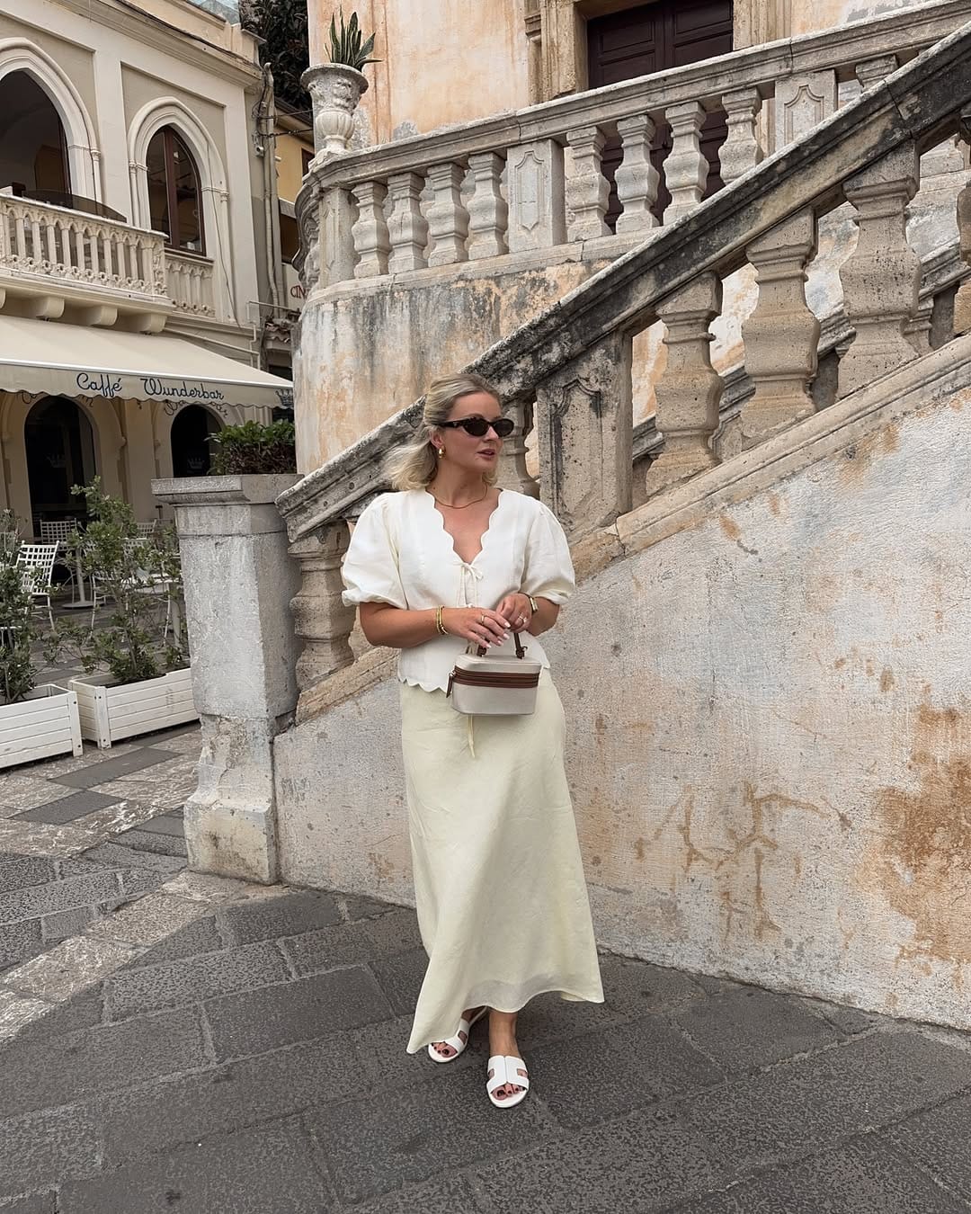 White linen puff-sleeve scallop blouse and cream satin midi skirt with white mules on an Italian street