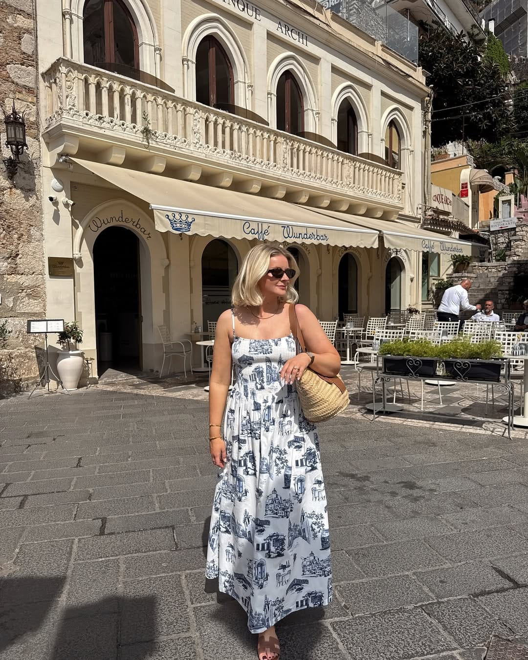 White and navy toile de Jouy maxi dress with straw bag and sunglasses in a Sicilian piazza, Italy outfit