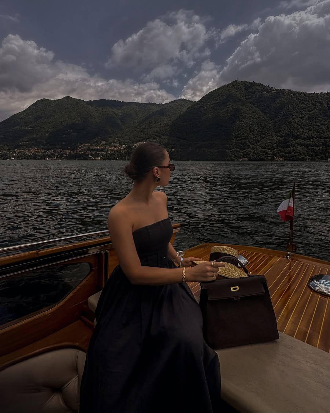 Black strapless silk gown on wooden speedboat on Lake Como with Italian flag, Italian summer outfit idea