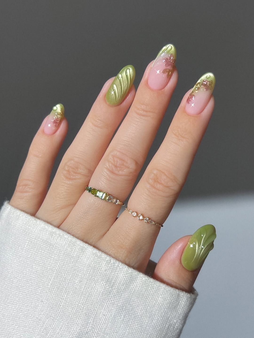 Olive green chrome almond nails with 3D swirl design and pink gemstone tips