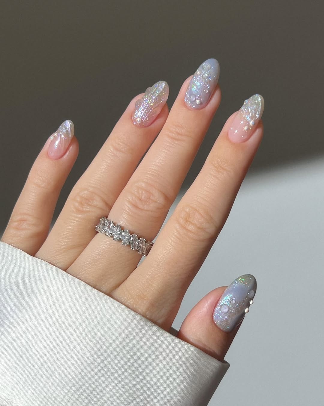 Sheer periwinkle almond nails with holographic glitter tips and pearl clusters
