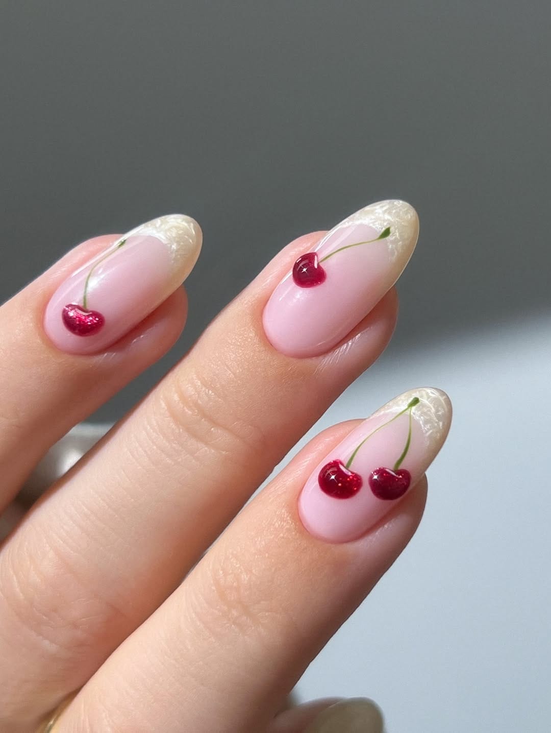 Sheer almond nails with pearl French tips and glitter cherry accents