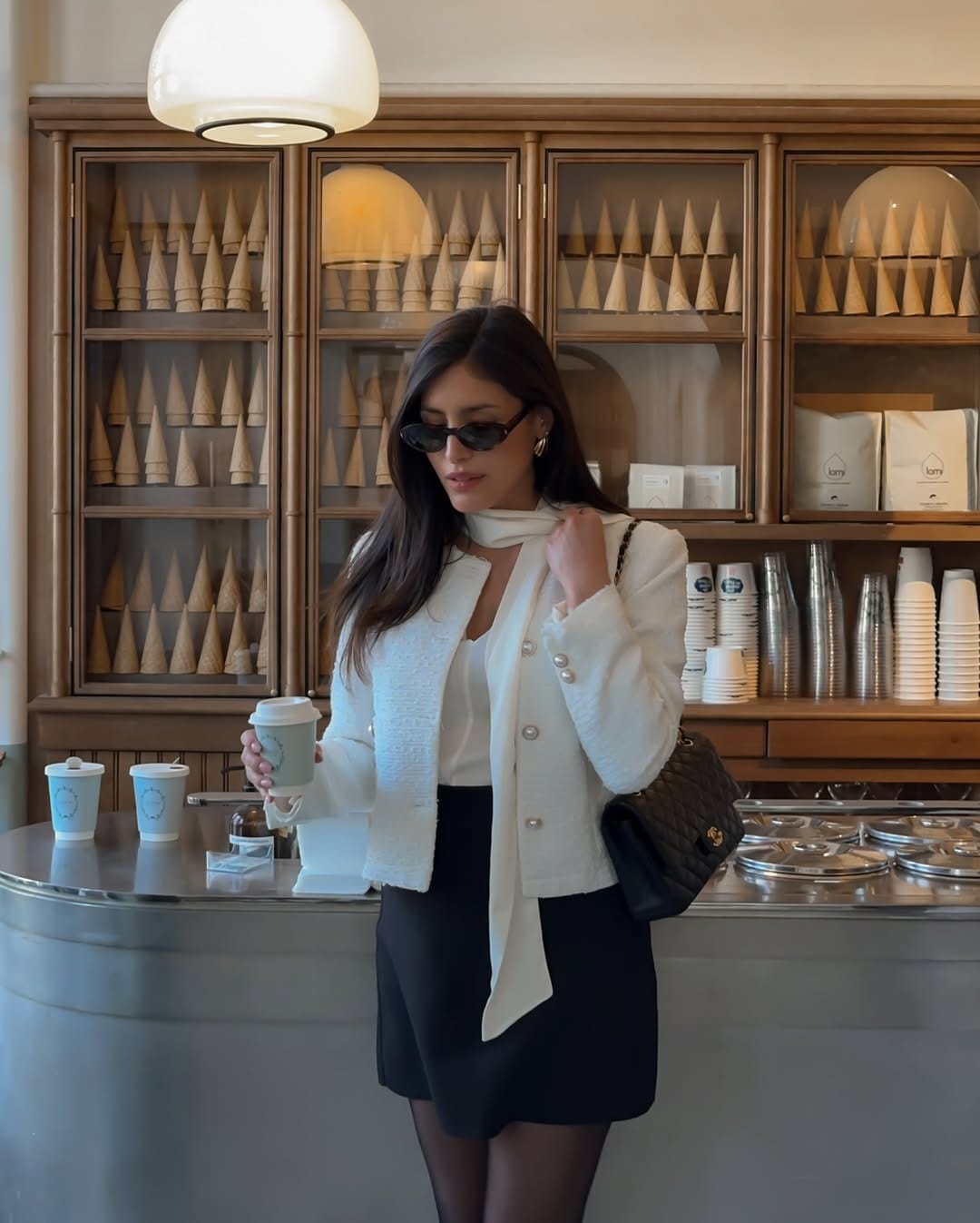 White tweed jacket with pearl buttons paired with a black mini skirt and neck scarf