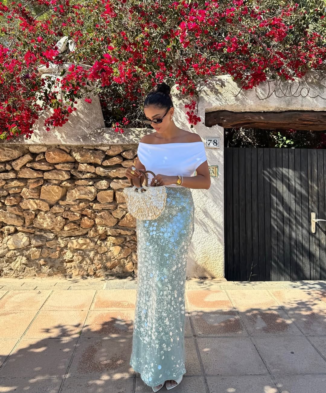 White off-shoulder top with a blue sequin maxi skirt and crochet bag for a festival-ready look.
