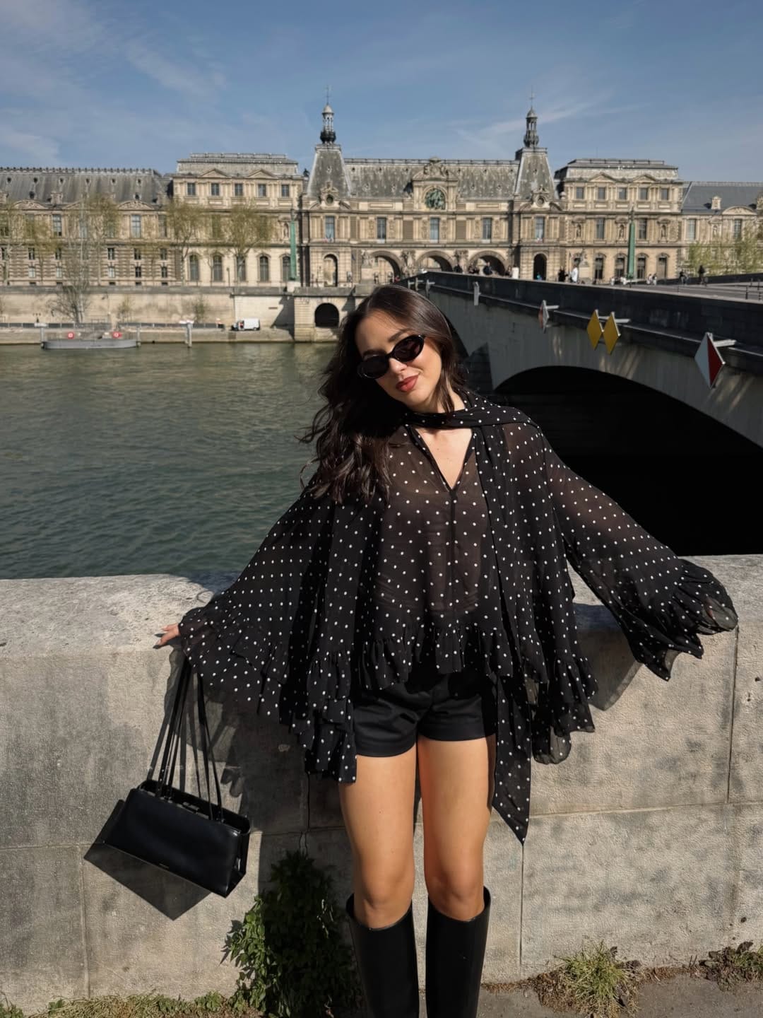 Black sheer polka dot ruffle blouse with leather shorts and knee-high boots for an edgy concert look.