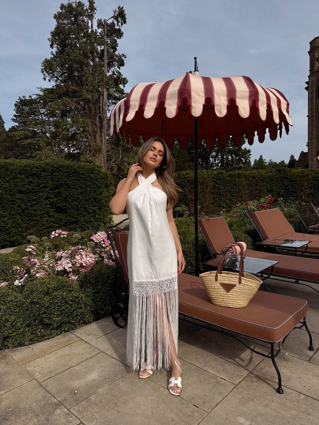 White linen halter maxi dress with fringe hem and straw tote for a relaxed summer festival vibe.