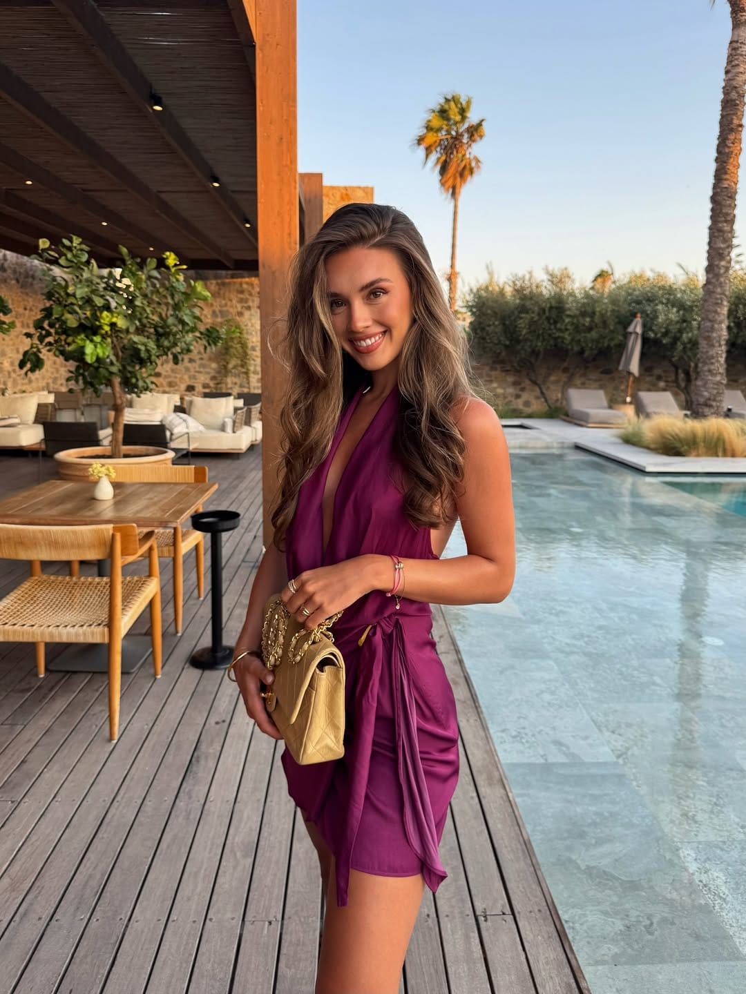 Magenta halter wrap mini dress with a gold bag for a bold summer concert outfit.