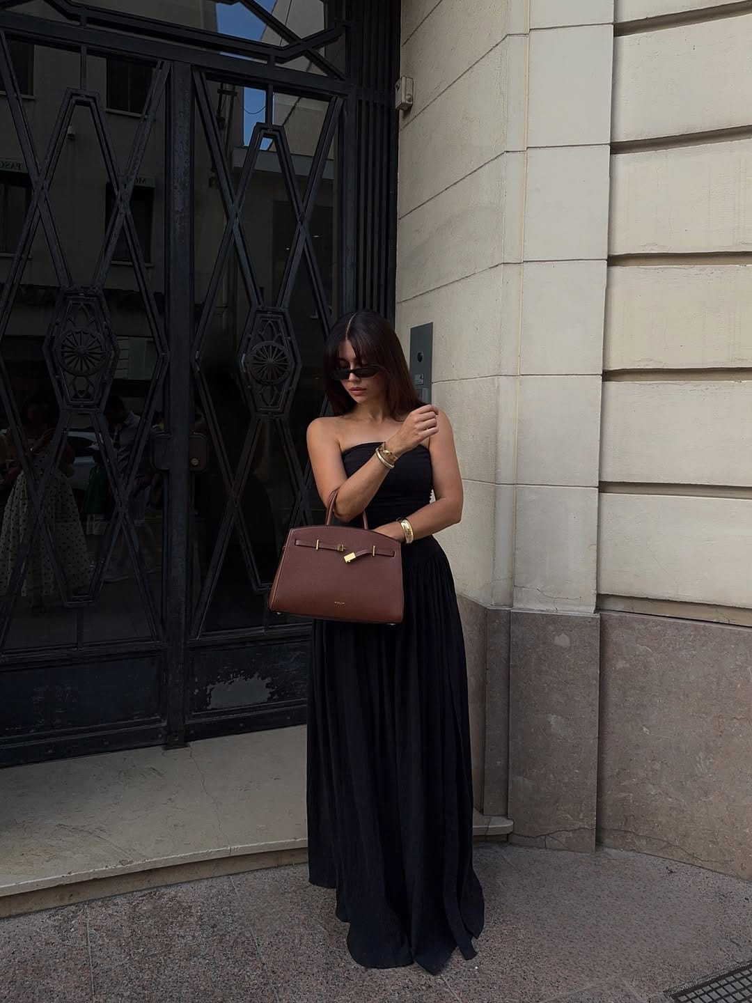 Black strapless pleated maxi dress styled with a cognac tote bag
