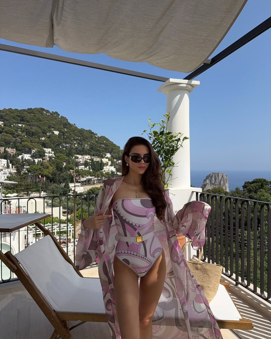 A pink paisley print swimsuit layered with a matching sheer kimono and a raffia tote for a coordinated resort style.