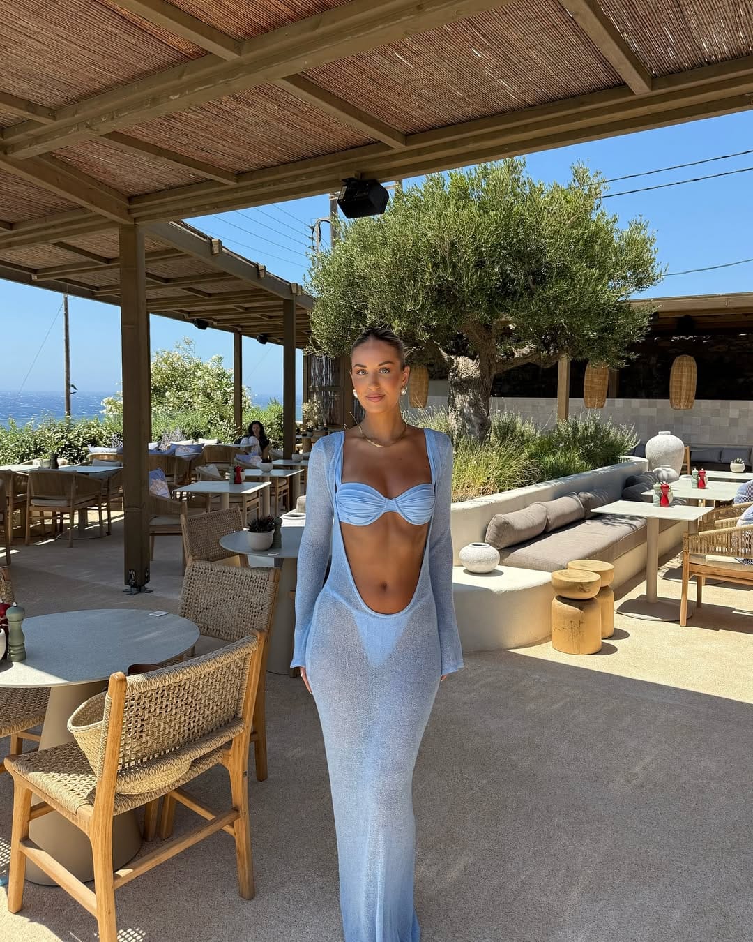 A powder blue ruched bikini top paired with a sheer knit maxi skirt and an open cardigan for a layered beach ensemble.