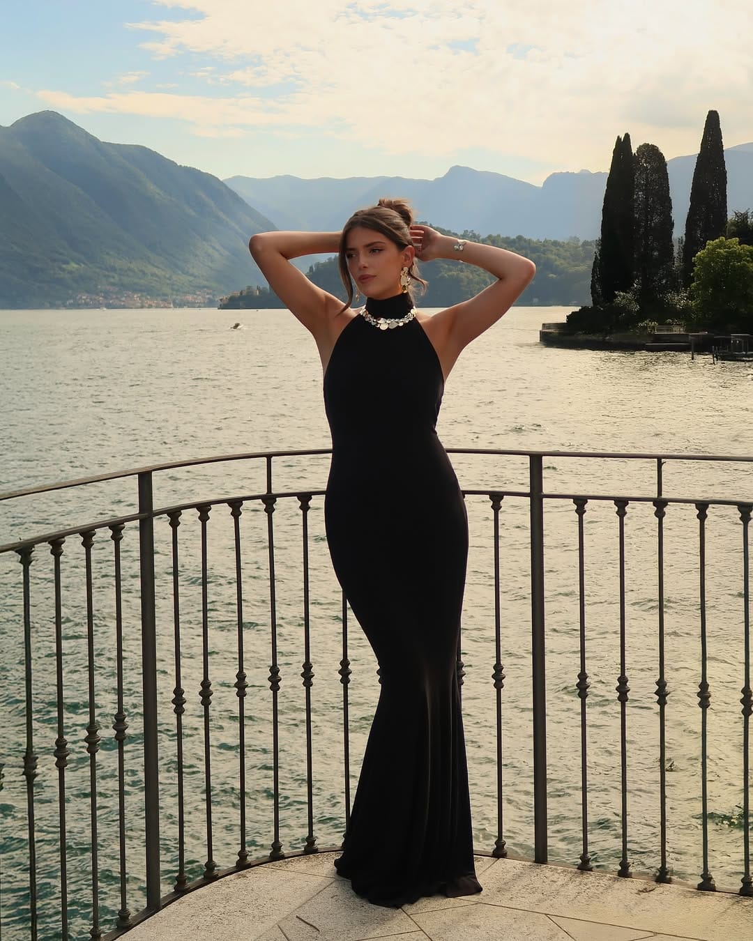 A sleek black halter neck jersey column gown styled with a bold gold coin choker for an elevated evening look.